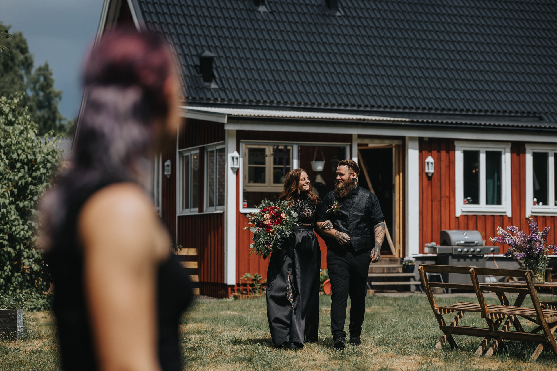 Nygift brudpar promenerar tillsammans i trädgården utanför sitt röda hus i Hässleholm