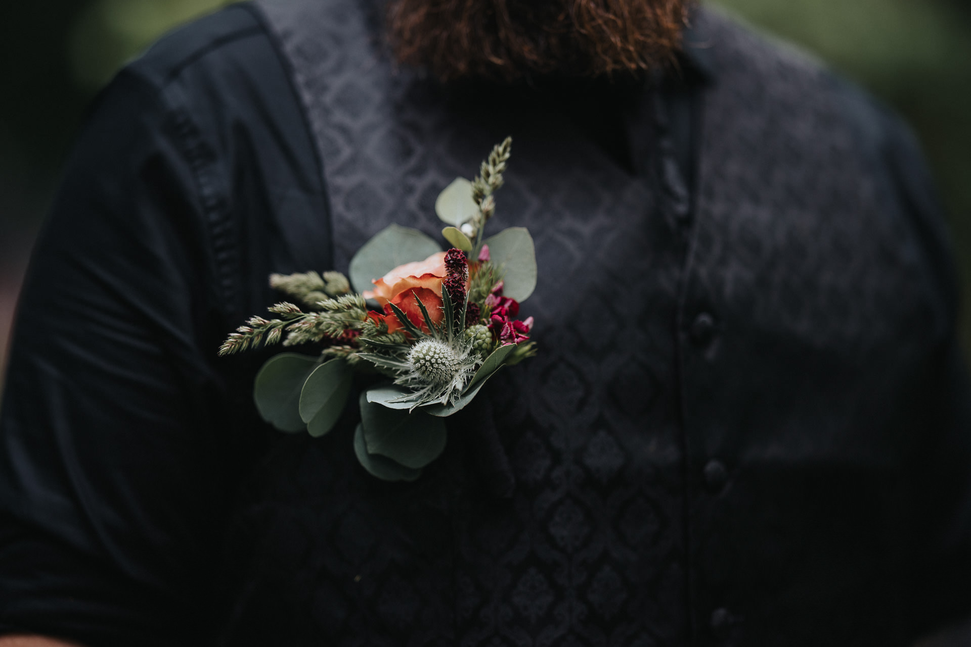 Närbild på brudgummens mörka mönstrade väst och blomsterdekoration vid ett personligt trädgårdsbröllop